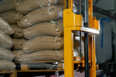 Kahve fabrikasındaki bir işçiyi kapatmak için sarı bir forklift kullanır ve rafa bir palet koyar.