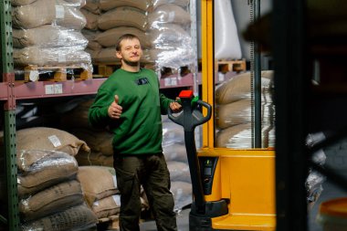 Kahve fabrikasında çalışan bir işçi, arkasında sarı forklift taşıyan bir adam kahve torbaları taşıyor.