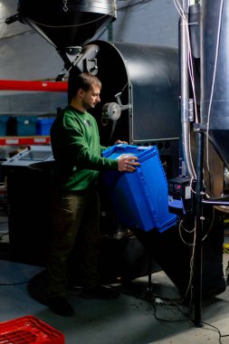 Kahve fabrikasındaki işçiler mavi kutudan kahve kızartma mekanizmasına yeşil kahve dökerler.