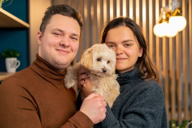 Birbirine aşık bir çift ayakta dikiliyor ve bir köpeğe sıkıca sarılıyor. Yulaf lapasında aile fotoğraflarında sıkıca tutuyor.