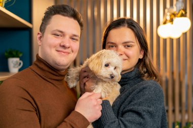 Birbirine aşık bir çift ayakta dikiliyor ve bir köpeğe sıkıca sarılıyor. Yulaf lapasında aile fotoğraflarında sıkıca tutuyor.