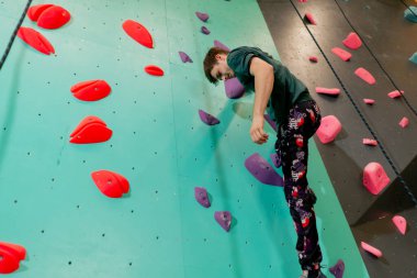 Tırmanma duvarının altında genç ve yakışıklı bir antrenör sigortasız duvara tırmanıyor.