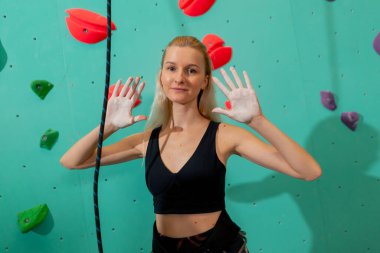 Tırmanma duvarında genç bir kız kameraya poz vererek ilk kaya tırmanışı denemesinden sonra mutlu olur.