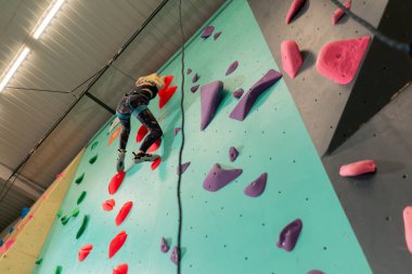 tırmanma duvarında genç bir kız ilk kez duvara tırmanıyor, koç emniyet halatıyla bağlanıyor.