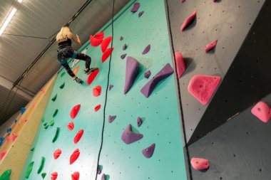 tırmanma duvarında genç bir kız emniyet halatından iniyor, koç düşmeye karşı sigorta yaptırıyor.