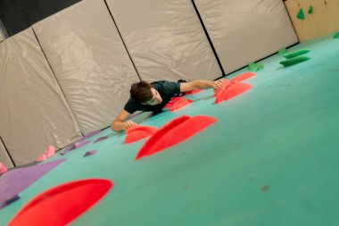 Tırmanma duvarının tepesinde genç ve yakışıklı bir antrenör sigortasız duvara tırmanıyor.