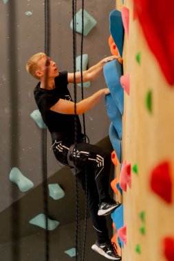 Tırmanma duvarının tepesinde genç ve yakışıklı bir antrenör sigortasız duvara tırmanıyor.
