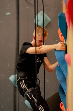 Tırmanma duvarının tepesinde genç ve yakışıklı bir antrenör sigortasız duvara tırmanıyor.