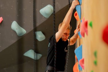 Tırmanma duvarının tepesinde genç ve yakışıklı bir antrenör sigortasız duvara tırmanıyor.