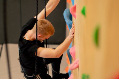 Tırmanma duvarının tepesinde genç ve yakışıklı bir antrenör sigortasız duvara tırmanıyor.