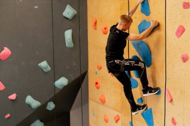 Tırmanma duvarının tepesinde genç ve yakışıklı bir antrenör sigortasız duvara tırmanıyor.