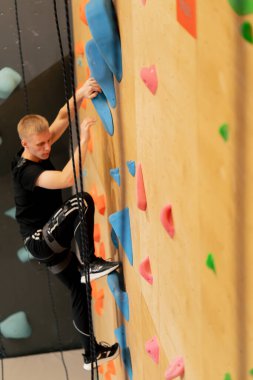 Tırmanma duvarının tepesinde genç ve yakışıklı bir antrenör sigortasız duvara tırmanıyor.