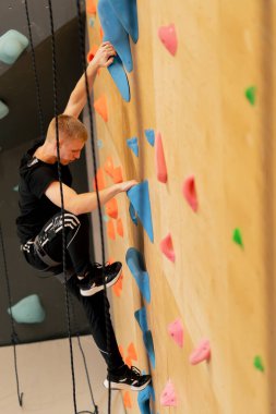 Tırmanma duvarının tepesinde genç ve yakışıklı bir antrenör sigortasız duvara tırmanıyor.