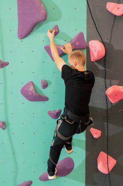 Tırmanma duvarında genç ve yakışıklı bir antrenör sigortası olmadan duvara tırmanıyor.