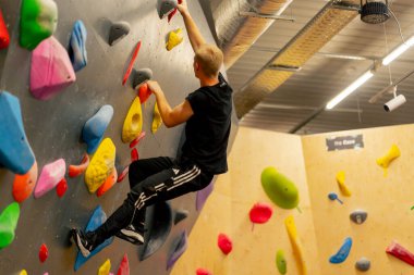 Tırmanma duvarına yakın çekim yapan genç, yakışıklı, profesyonel bir antrenör sigortası olmadan duvara tırmanır.