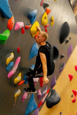 Tırmanma duvarına yakın çekim yapan genç, yakışıklı, profesyonel bir antrenör sigortası olmadan duvara tırmanır.