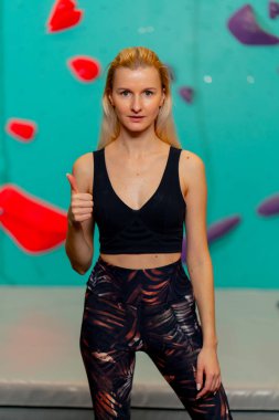 Tırmanma duvarında genç bir kız kameraya poz vererek ilk kaya tırmanışı denemesinden sonra mutlu olur.