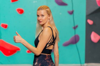 Tırmanma duvarında genç bir kız kameraya poz vererek ilk kaya tırmanışı denemesinden sonra mutlu olur.