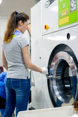 Profesyonel kuru temizlemeci kız çamaşır makinesini açar.