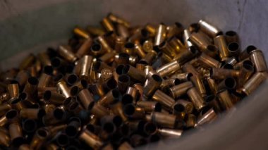 Profesyonel bir atış poligonunda yakın plan bir kovaya bir sürü kullanılmış mermi konteynıra dökülüyor.