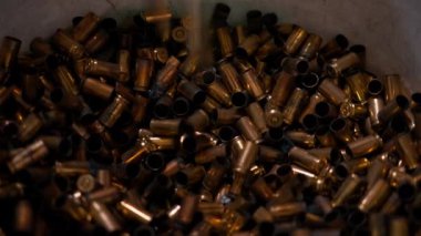 Profesyonel bir atış poligonunda yakın plan bir kovaya bir sürü kullanılmış mermi konteynıra dökülüyor.