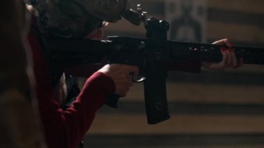Profesyonel bir atış poligonunda taktik cephaneli ucuz bir kız ateş ediyor.