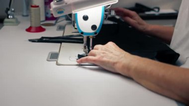 Bir makinenin dikiş atölyesinde kapanıyor yaşlı terzi kadın siyah bir kumaşı kesiyor.
