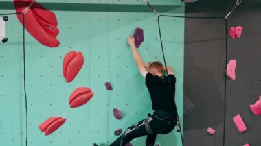 Tırmanma duvarının tepesinde genç ve yakışıklı bir antrenör sigortasız duvara tırmanıyor.