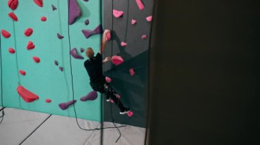 Tırmanma duvarının tepesinde genç ve yakışıklı bir antrenör sigortasız duvara tırmanıyor.