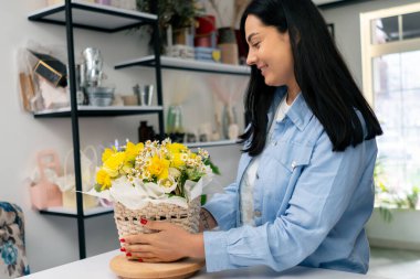 Bir çiçekçide bir çiçekçi, sepetteki sarı çiçeklerle tamamlanmış bir çiçek düzenine hayran kalır.