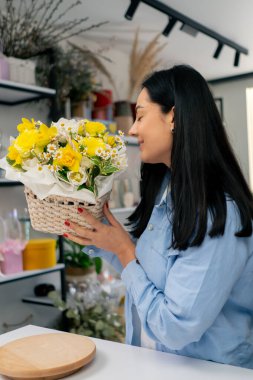 Bir çiçekçide bir çiçekçi, sepetteki sarı çiçeklerle tamamlanmış bir çiçek düzenine hayran kalır.
