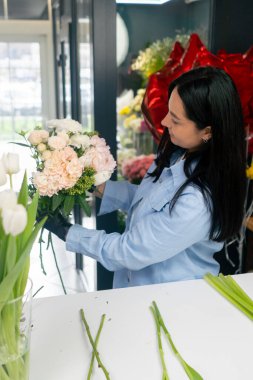 Çiçekçi bir kız beyaz bir masanın yanında güzel bir buket beyaz çiçek topluyor.