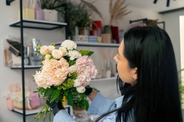 Çiçekçi bir kız beyaz bir masanın yanında güzel bir buket beyaz çiçek topluyor.