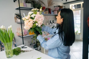 Çiçekçi bir kız beyaz bir masanın yanında güzel bir buket beyaz çiçek topluyor.