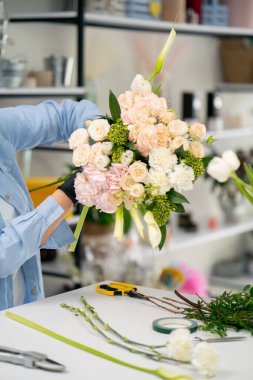 Çiçekçi bir kız beyaz bir masanın yanında güzel bir buket beyaz çiçek topluyor.