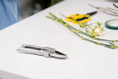 Beyaz bir masanın üzerindeki çiçekçi dükkanında çiçekleri kesmek için budama makası var.