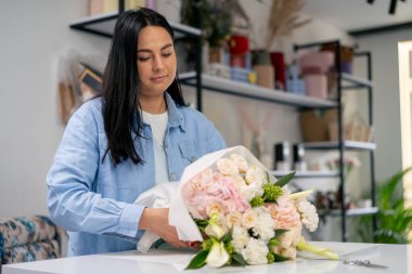 Çiçekçide bir çiçekçi hazır narin bir buketi beyaz bir kağıda sarar.