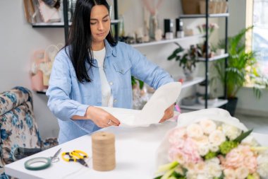 Çiçekçide bir çiçekçi hazır narin bir buketi beyaz bir kağıda sarar.