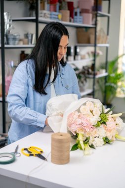 Çiçekçide bir çiçekçi hazır narin bir buketi beyaz bir kağıda sarar.