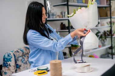 Bir çiçekçide bir çiçekçi tamamlanmış bir çiçek aranjmanına menekşe bir kurdele bağlar.