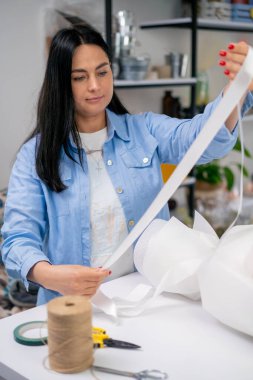 Bir çiçekçide çiçekçi, tamamlanmış bir çiçek aranjmanına beyaz bir kurdele bağlar.