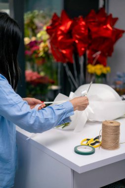 Bir çiçekçide çiçekçi, tamamlanmış bir çiçek aranjmanına beyaz bir kurdele bağlar.