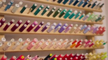 Dikiş atölyesinde, duvardaki bir standın üzerinde farklı renkte iplik izleri var.