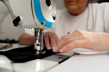 Bir makinenin dikiş atölyesinde kapatılıyor. Terzi kadın siyah bir kumaşı kesiyor.