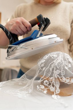 Bir dikiş atölyesinde bir kadın, profesyonel bir ütüyle gelin için dantel bir peçe ütüler.