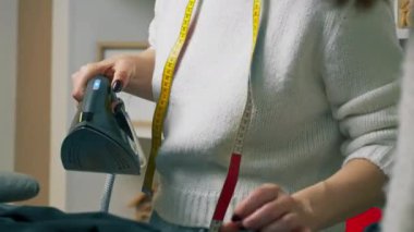 Bir dikiş atölyesinde. Yırtılma için siyah kumaş ütüleyen bir terzi.