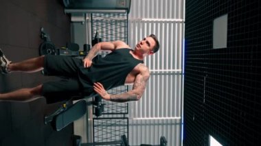 Spor salonunda siyah tişörtlü yakışıklı adam egzersiz makinesinin önünde ısınma egzersizi yapıyor.