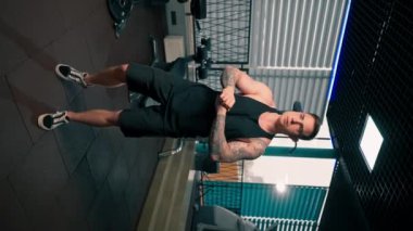 Spor salonunda siyah tişörtlü yakışıklı adam egzersiz makinesinin önünde ısınma egzersizi yapıyor.