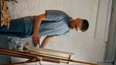 dikey video mavi tişörtlü sakallı genç bir sanatçı tuvalde büyük bir fırçayla yazıyor.