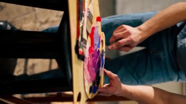 Bir sanat stüdyosunda dikey video bir sanatçı palet üzerine palet bıçağıyla boya karıştırır.